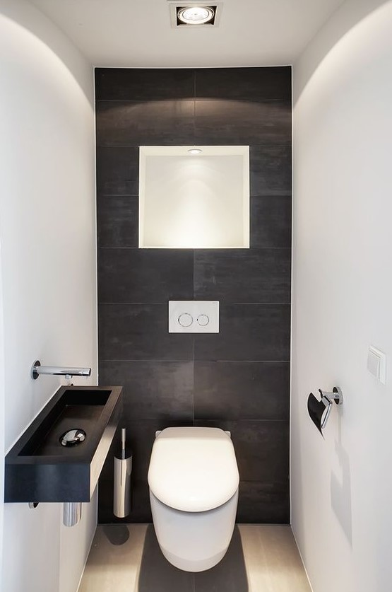 a minimalist guest bathroom with black and white tiles of different sizes, a black wall-mounted sink and some lights