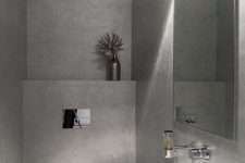 a minimalist guest toilet done with concrete, a wall-mounted sink, a lamp and a large mirror