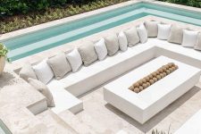 a minimalist neutral sunken fire pit with a built-in bench with lots of pillows and a fireplace in the center plus a narrow pool around