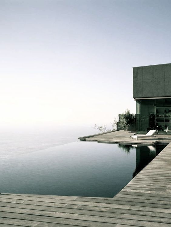 a minimalist outdoor space with an infinity pool, a sea view, a wooden deck and a lounger is a beautiful and super chic space