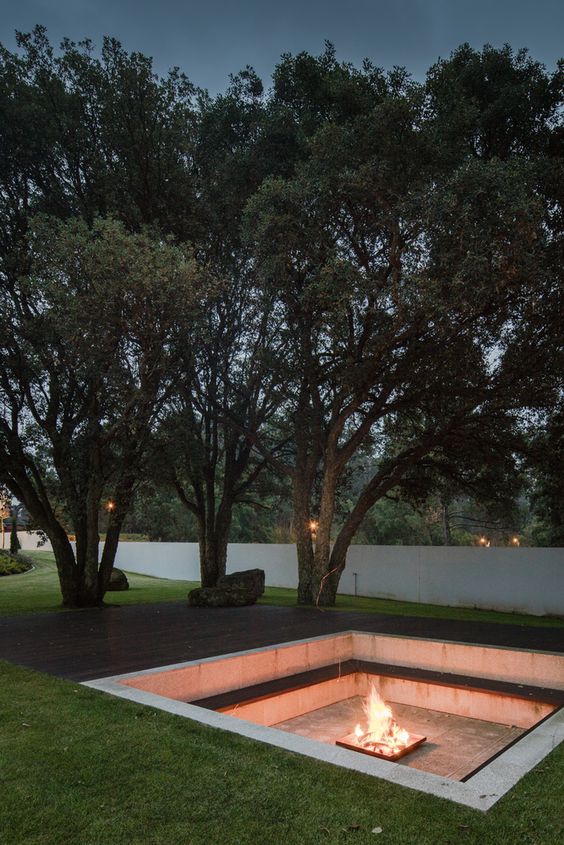 a minimalist outdoor sunken fire pit wiht a built-in bench along the perimeter and a fire pit in the center of this pit