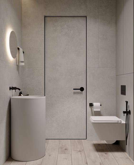a minimalist powder room clad with grey stone tiles, with a whitewashed floor, a grey free-standing sink and a round mirror, a floating toilet