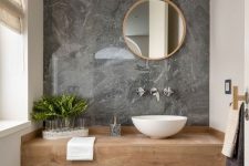 a minimalist powder room with grey stone tiles, a floating vanity, a round mirror, greenery and a neutral toilet
