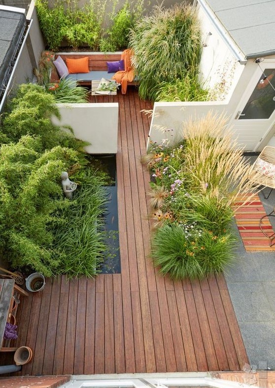 a minimalist townhouse garden with a wooden deck, a pond, planted herbs and grasses and a built in bench
