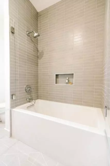 a modern bathroom with greige skinny tiles, a white tub and a niche shelf is a stylish bathroom space