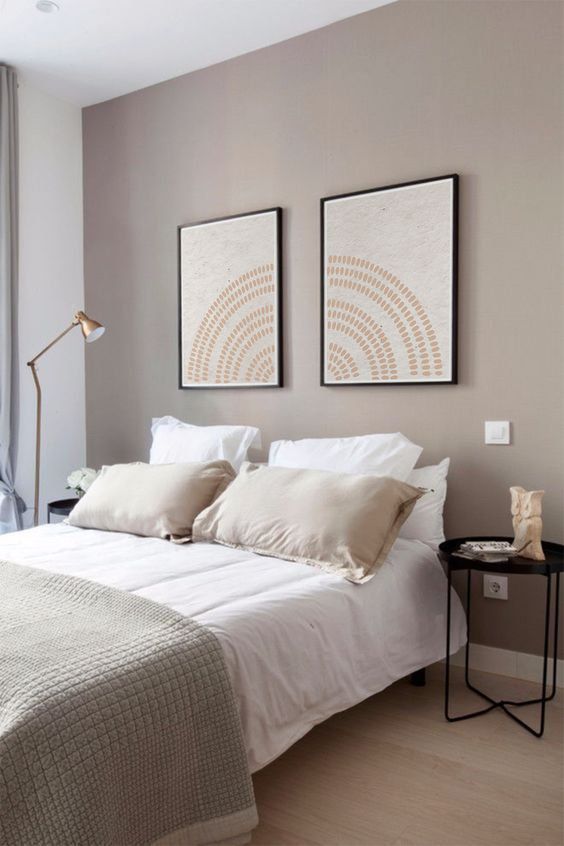 a modern bedroom with a greige accent wall, a bed with neutral bedding, artwork, black nightstands and floor lamps