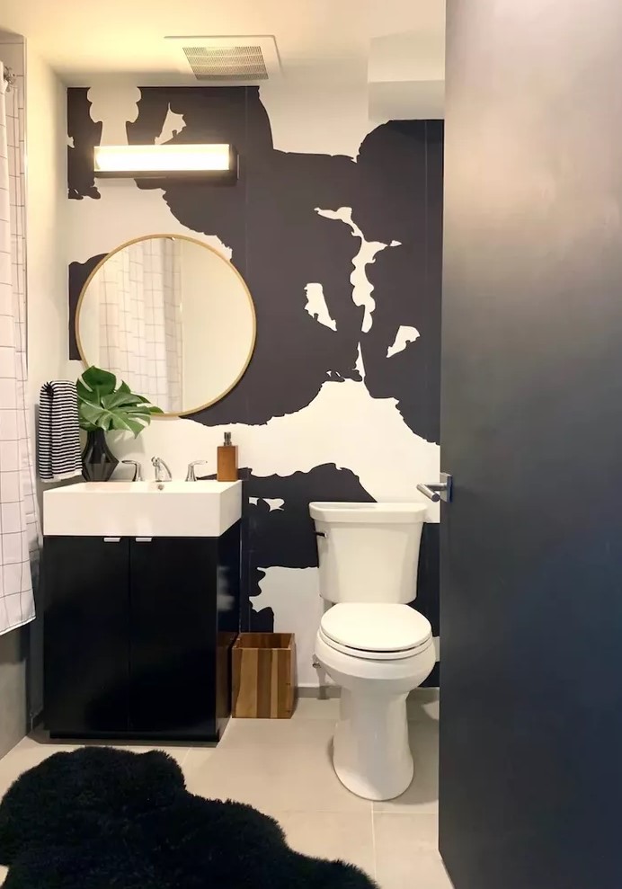 a modern black and white powder room with catchy wallpaper, a black vanity with a white sink and a round mirror