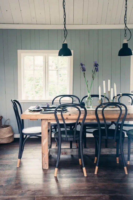 a modern country dining room with blue walls, a stained wooden table, black chairs, vintage black pendant lamps