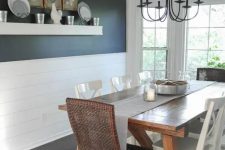 a modern farmhouse dining room with a black wall and white planks, a stained dining table, mismatching chairs and a vintage chandelier
