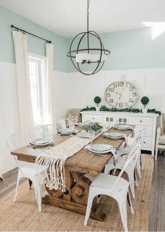 a modern farmhouse dining room with blue and white paneled walls, a stained vintage dining table, white metal chairs, a sphere chandelier