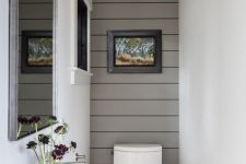 a modern farmhouse powder room wiht a grey planked wall, white appliances, artwork and a black lamp is a chic space