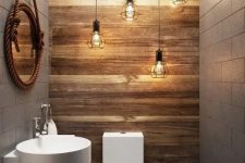 a modern industrial powder room with a cluster of pendant bulbs, a wall-mounted sink and a toilet plus a mirror in rope