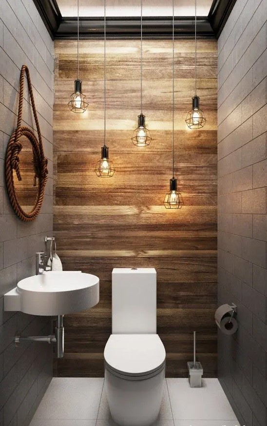 a modern industrial powder room with a cluster of pendant bulbs, a wall-mounted sink and a toilet plus a mirror in rope