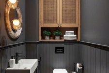 a modern moody powder room with grey walls, a cane storage cabinet, white appliances and a black vanity, pendant lamps