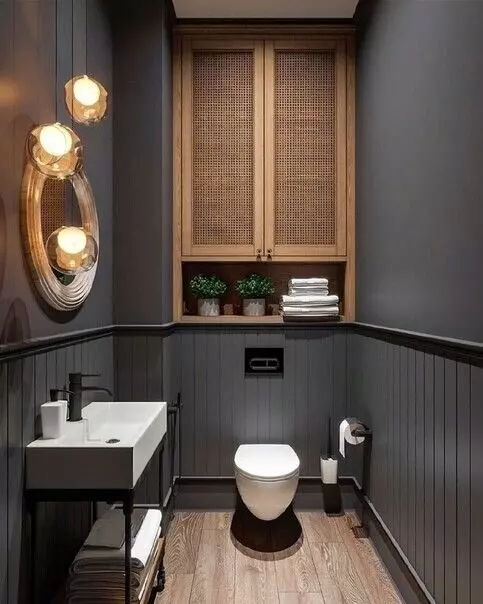 a modern moody powder room with grey walls, a cane storage cabinet, white appliances and a black vanity, pendant lamps