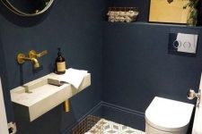 a modern moody powder room with navy walls, a white stone wall-mounted sink and a white toilet, a geo floor and a round mirror