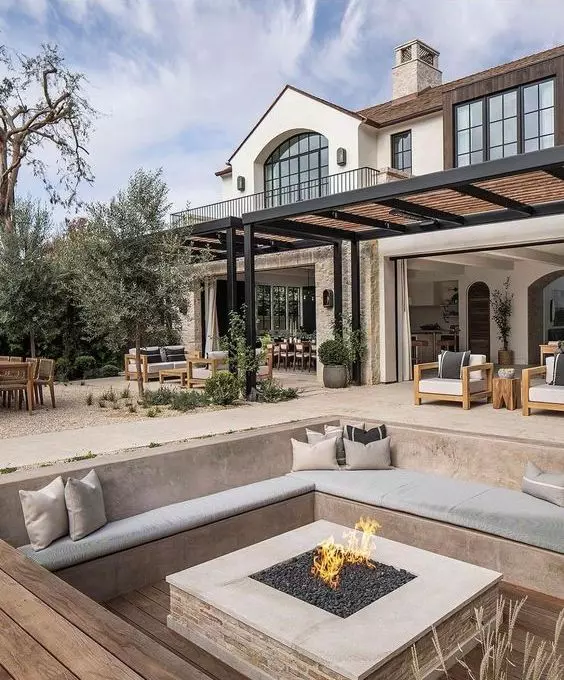 a modern neutral sunken patio with built-in benches and neutral upholstery, a fire pit in the center welcomes in