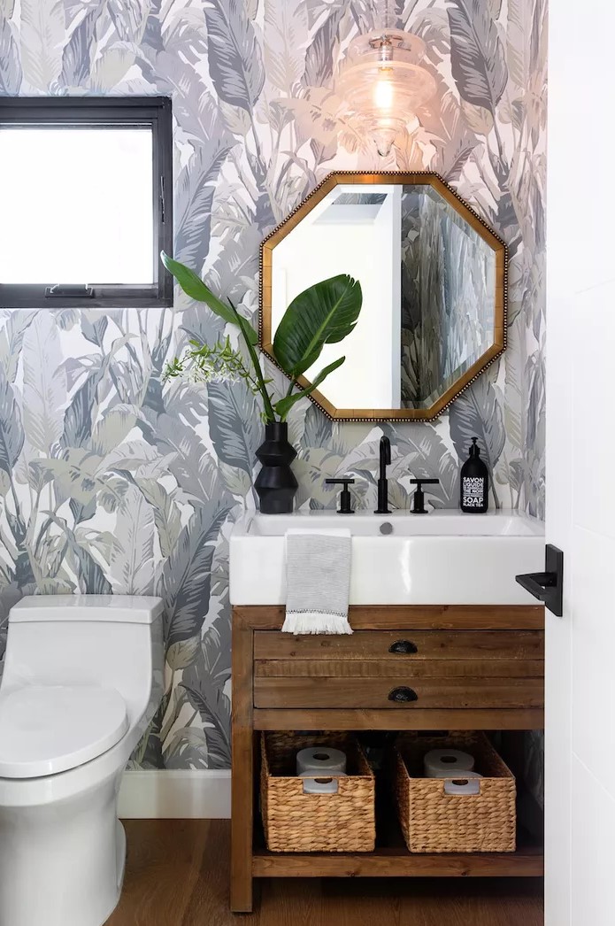 a modern powder room with blue printed wallpaper, a stained vanity with a sink, black fixtures and a hexagon mirror