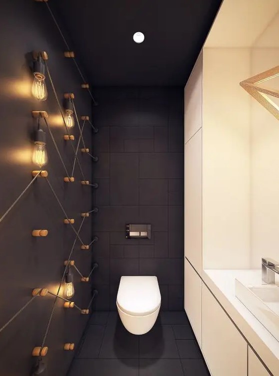 a modern powder room with industrial touches - bulbs on the wall, black tiles and a white storage unit