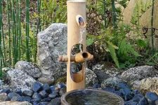 a modern take on a traditional Japanese bamboo fountain with a stone bowl and rocks around plus greenery