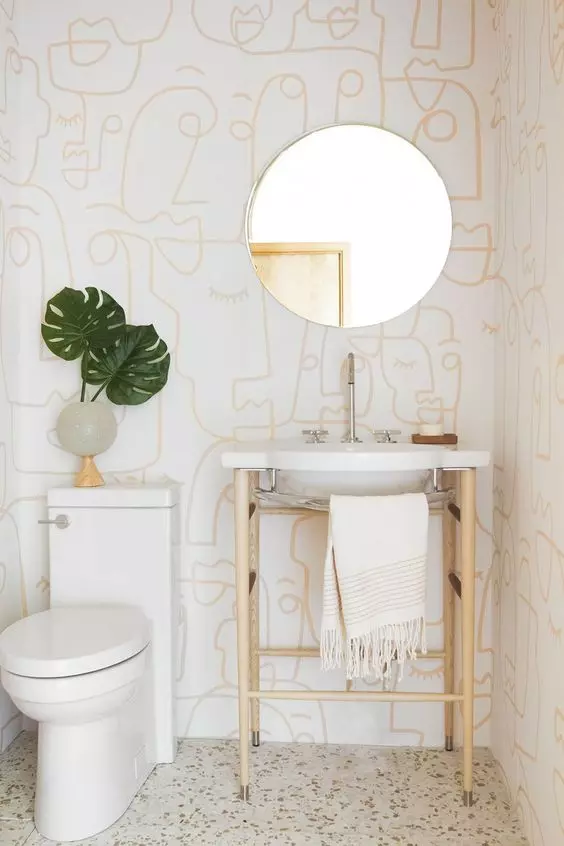 a modern to boho powder room with printed wallpaper, a sink on a stand, a round mirror and a catchy vase with leaves
