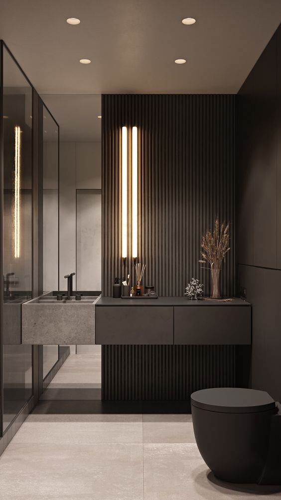 a moody minimalist powder room with a black wood slat wall, a mirror, a stone sink and a black toilet plus lights