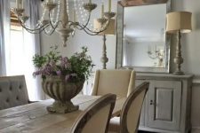 a neutral French farmhouse dining room with a vintage dining set, upholstered chairs, a whitewashed sideboard, vintage lamps and a crystal chandelier