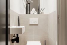 a neutral contemporary powder room clad with large scale tan tiles, a floating sink and a large mirror plus built-in lights