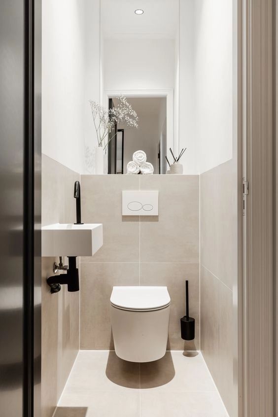 a neutral contemporary powder room clad with large scale tan tiles, a floating sink and a large mirror plus built-in lights