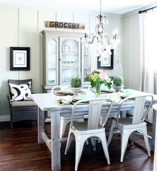 a neutral farmhouse dining area with whitewashed furniture, metal and wicker chairs, a sign and artworks