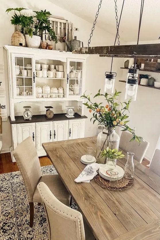 a neutral farmhouse dining room with a neutral buffet, a stained table, upholstered chairs, a vintage ladder with bulbs