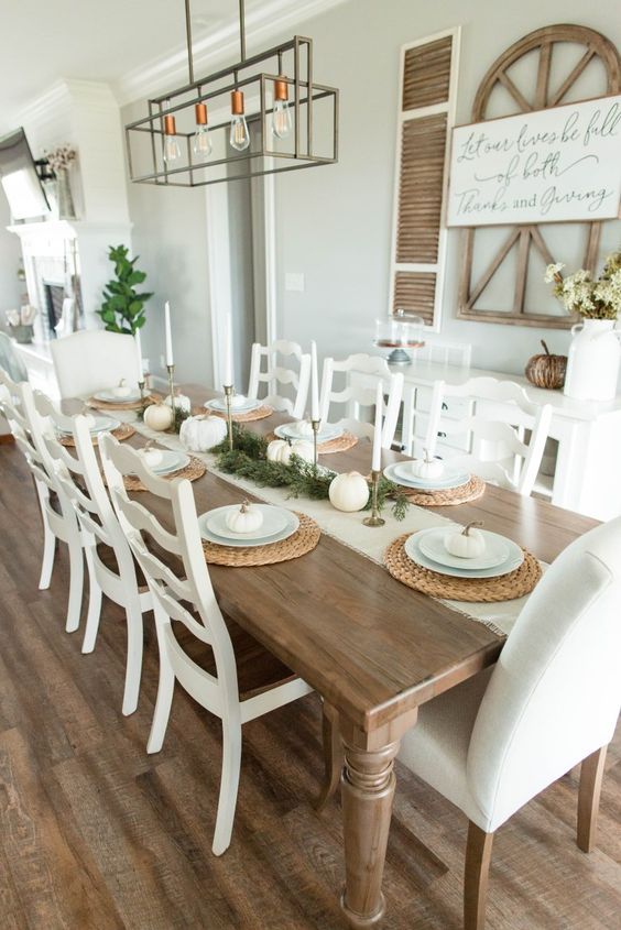 a neutral farmhouse dining space with a stained table and white chairs, a white credenza and some decor on the walls
