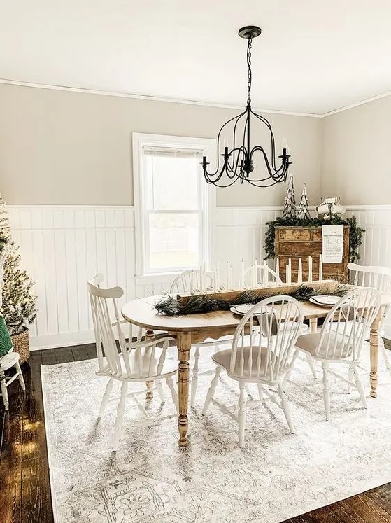 a neutral vintage farmhouse dining room with a curved table, white chairs, a metal chandelier and a wooden dresser