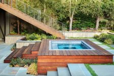 a partially recessed stainless steel spa features tile trim and a wooden deck around and greenery for a fresh touch