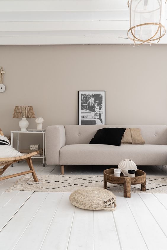a peaceful greige living room with a matching sofa, a chair, a carved wooden coffee table, an artwork and a printed rug