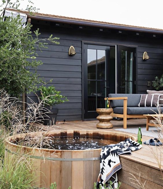 a pretty and welcoming wooden deck with a built-in tub, modern furniture and potted and just growing plants