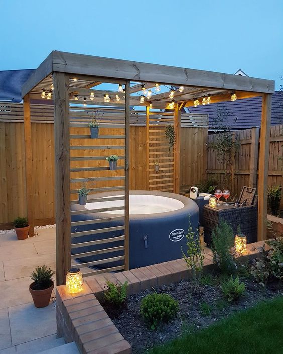 a pretty deck space with a hot tub, side tables, potted and growing plants and a bit of string lights and lanterns