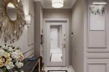 a refined greige entryway with a mirror door, a black marble console, a sunburst mirror and blooms plus a ceiling lamp