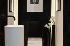 a refined minimalist powder room with black and white walls, a free-standing sink, a square toilet, some artwork and blooms