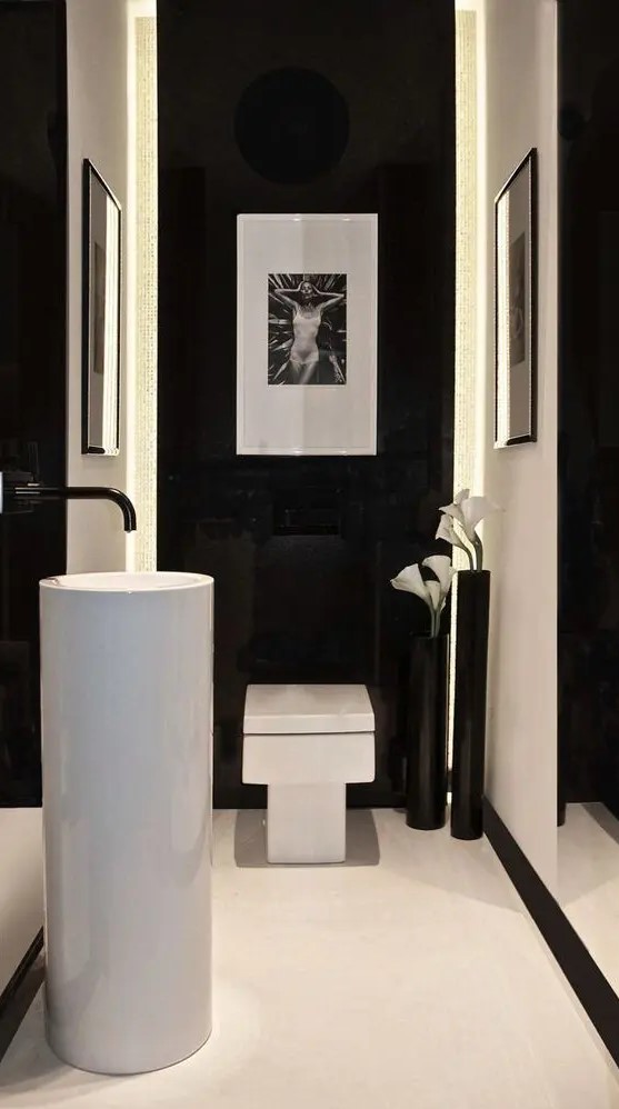 a refined minimalist powder room with black and white walls, a free-standing sink, a square toilet, some artwork and blooms