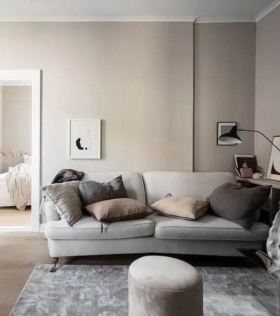 a relaxing greige living room with a grey sofa, muted color pillows, a bookshelf, some artworks and a black table lamp