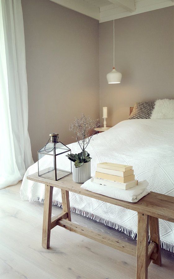 a serene greige bedroom with a bed with neutral bedding, a wooden bench and pendant lamps, some books and plants
