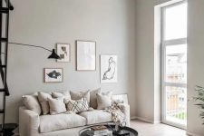 a serene greige living room with a neutral sofa, a round black coffee table and a side one, printed pillows and a small gallery wall
