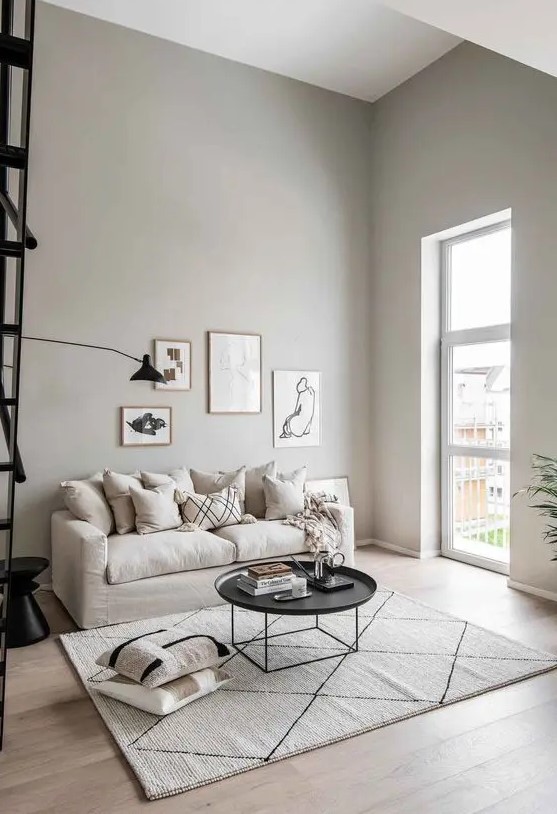 a serene greige living room with a neutral sofa, a round black coffee table and a side one, printed pillows and a small gallery wall