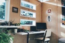 a she shed home office with timber walls, clerestory windows, a tiered desk, a white chair and greenery