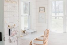 a she shed home office with white planked walls, a wooden bead chandelier, a white desk and a rattan chair, a prink printed rug