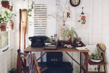 a she shed styled as a vintage working space with a stained desk and chairs, boxes for storage, potted greenery and blooms, oars and a clock