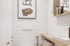 a simple and contemporary powder room with white and white tile walls, a mirror in a wooden frame, wooden shelves for storage and a sign