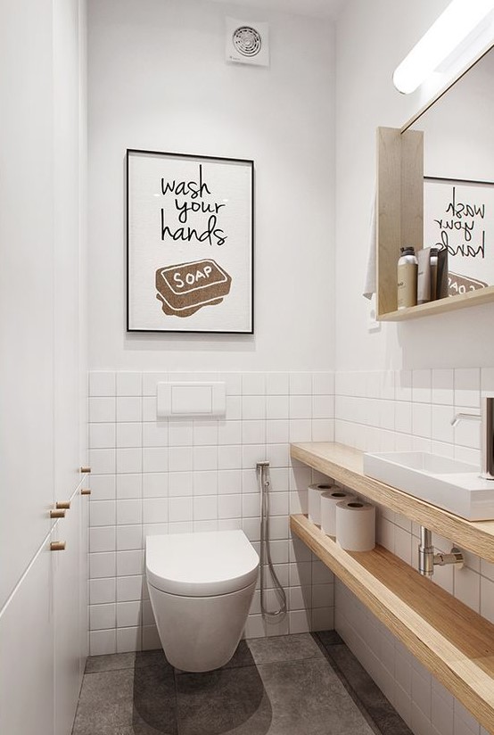 a simple and contemporary powder room with white and white tile walls, a mirror in a wooden frame, wooden shelves for storage and a sign