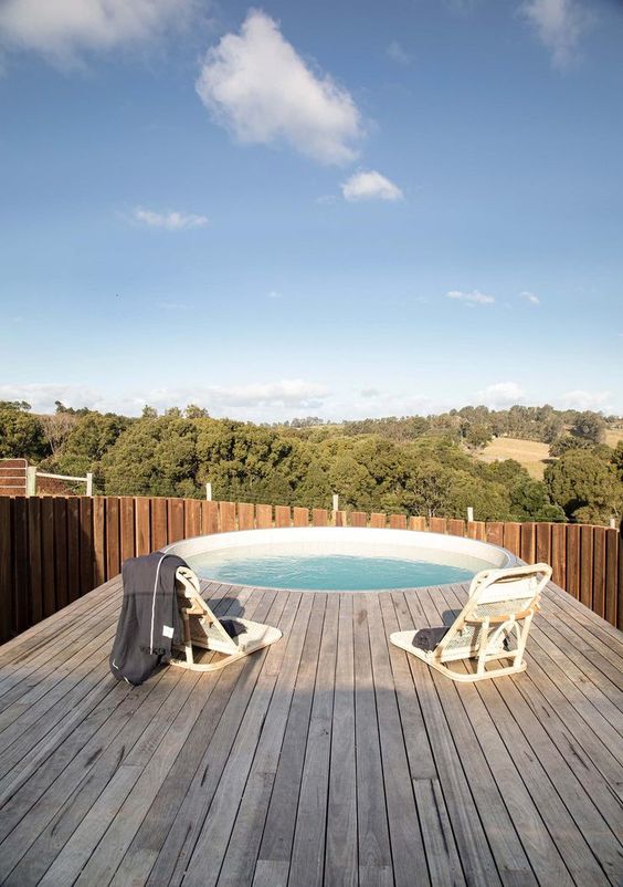 a simple modern outdoor space with a round pool, a wooden deck and white chairs is a lovely space to relax in